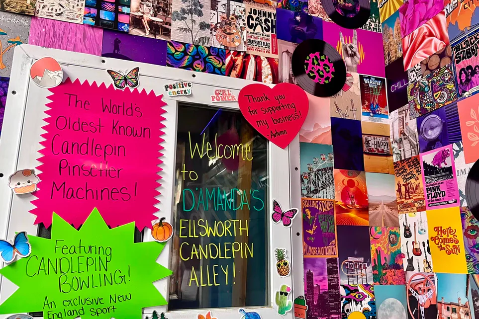A collage of colorful posters and hand-lettered signs beside a window at the alley.